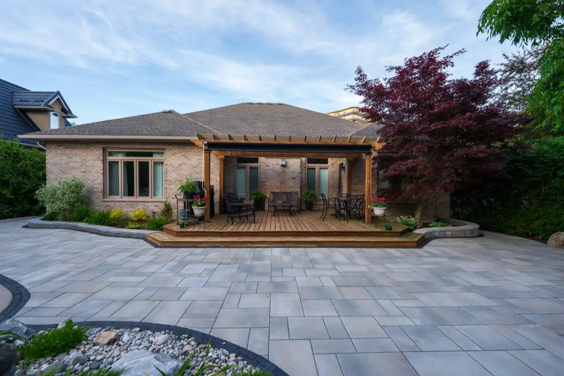 Pergola and paver patio behind a stone house at dusk