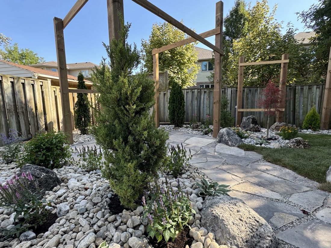 Upright juniper and perennials in a pebble bed beside flagstone