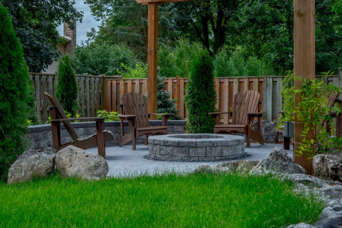 Adirondack chairs around a stone fire pit under a pergola