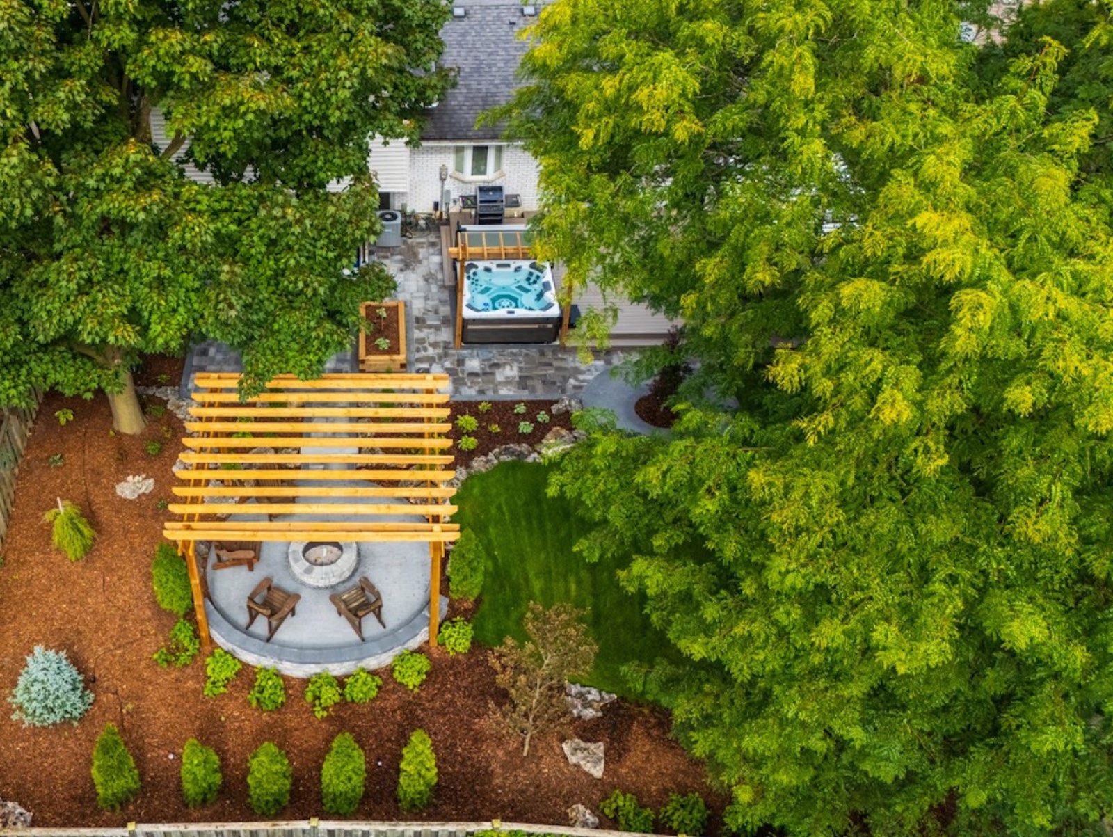 Aerial view of a finished backyard with cedar pergola, fire pit, and lush plantings