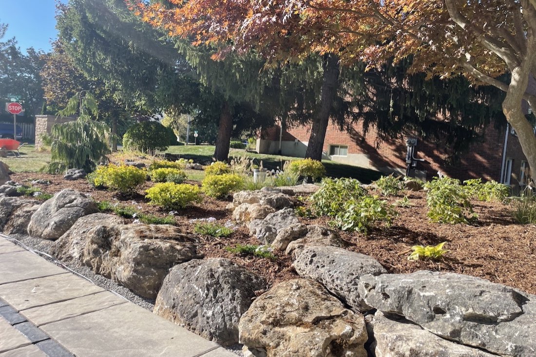 A custom rock-edged garden bed with shrubs and ornamental trees
