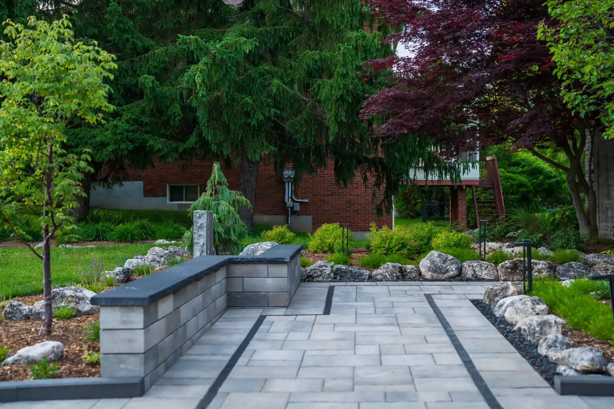 A paver courtyard with stone planter walls and path lighting at dusk
