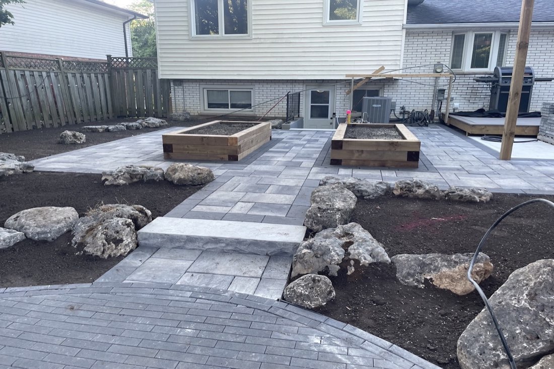 A large paver patio with armour-stone edging and cedar planters